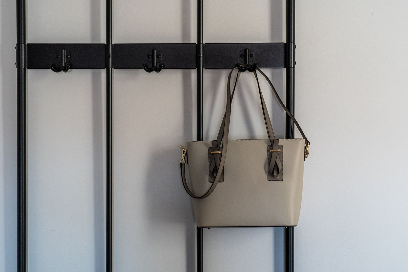 Stylish grey leather purse with gold details hanging on a modern black hook against a minimalist backdrop.