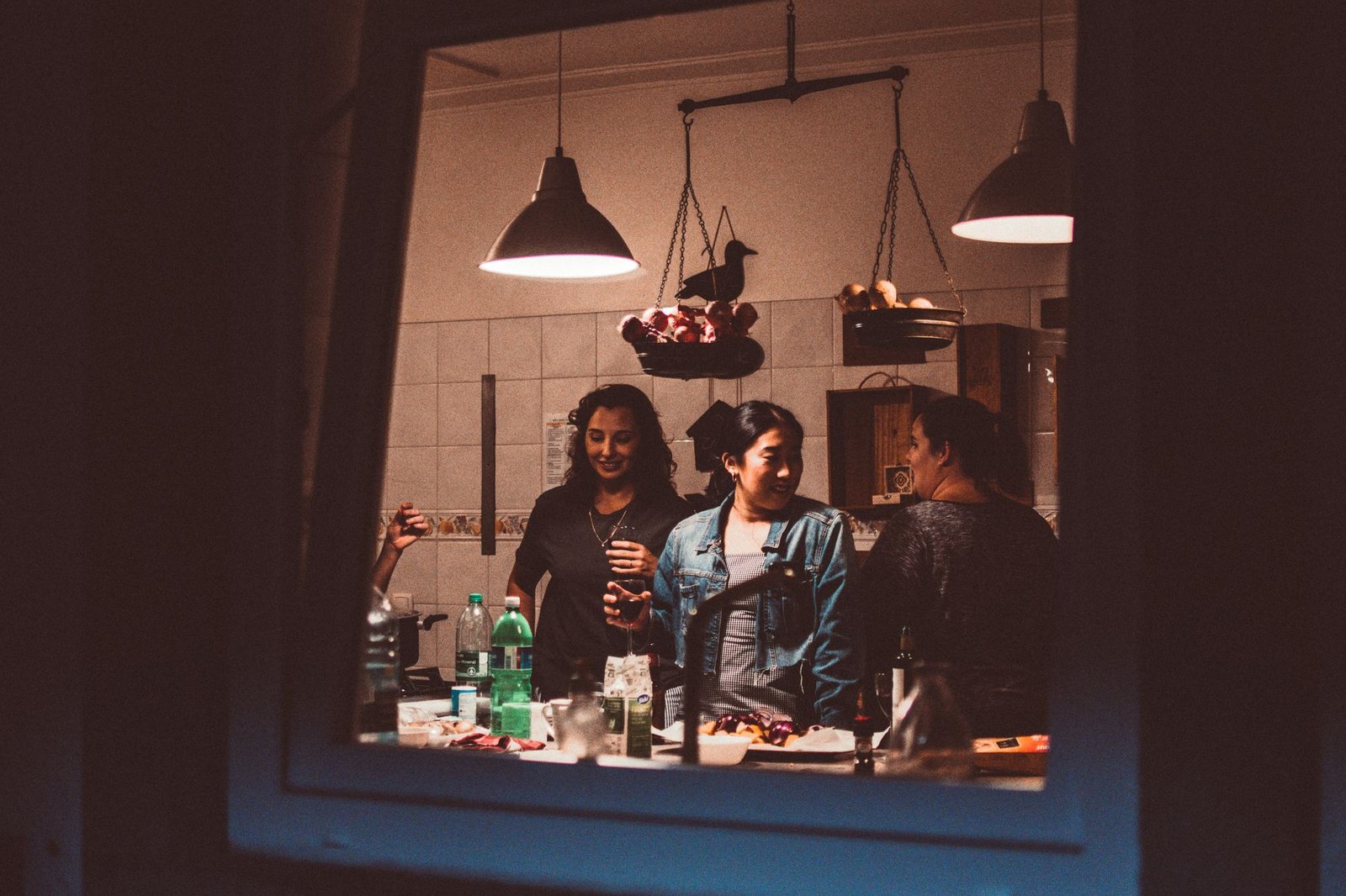 evening reset routine — A warm indoor gathering of friends in a kitchen, enjoying drinks and conversation at night.