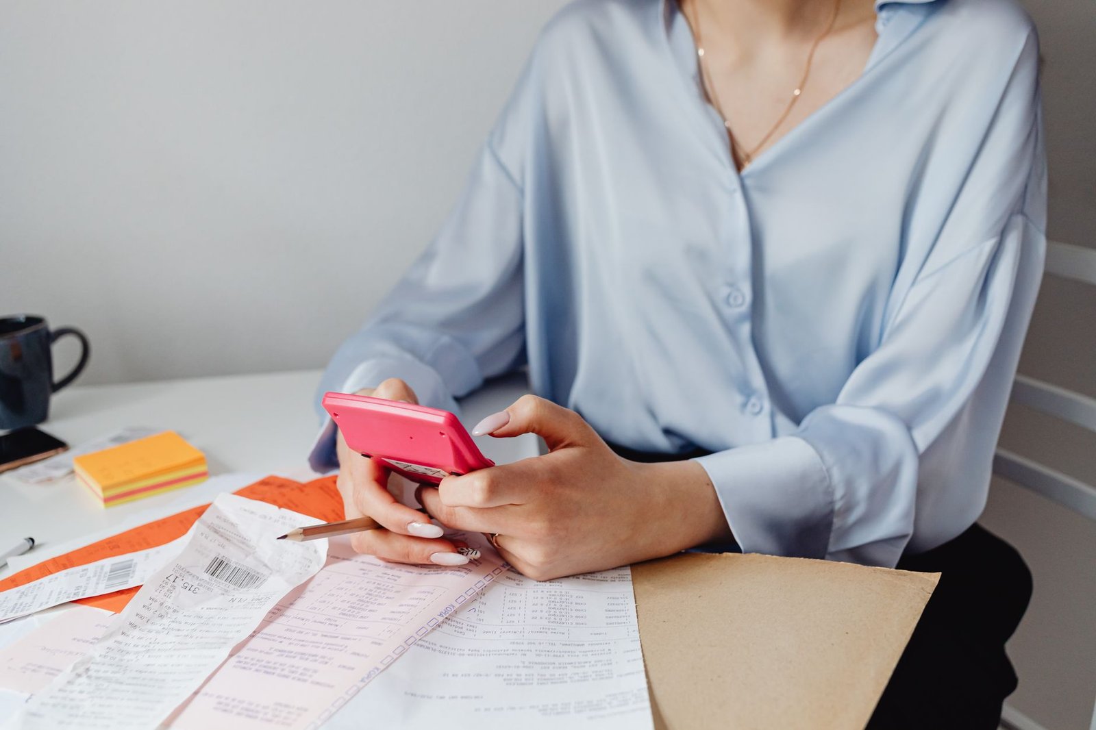 grocery budget — A woman using a pink calculator surrounded by bills and receipts at a desk.