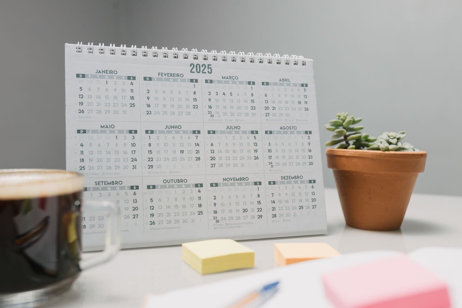 no spend month — A 2025 desk calendar with coffee, sticky notes, and succulents for planning.