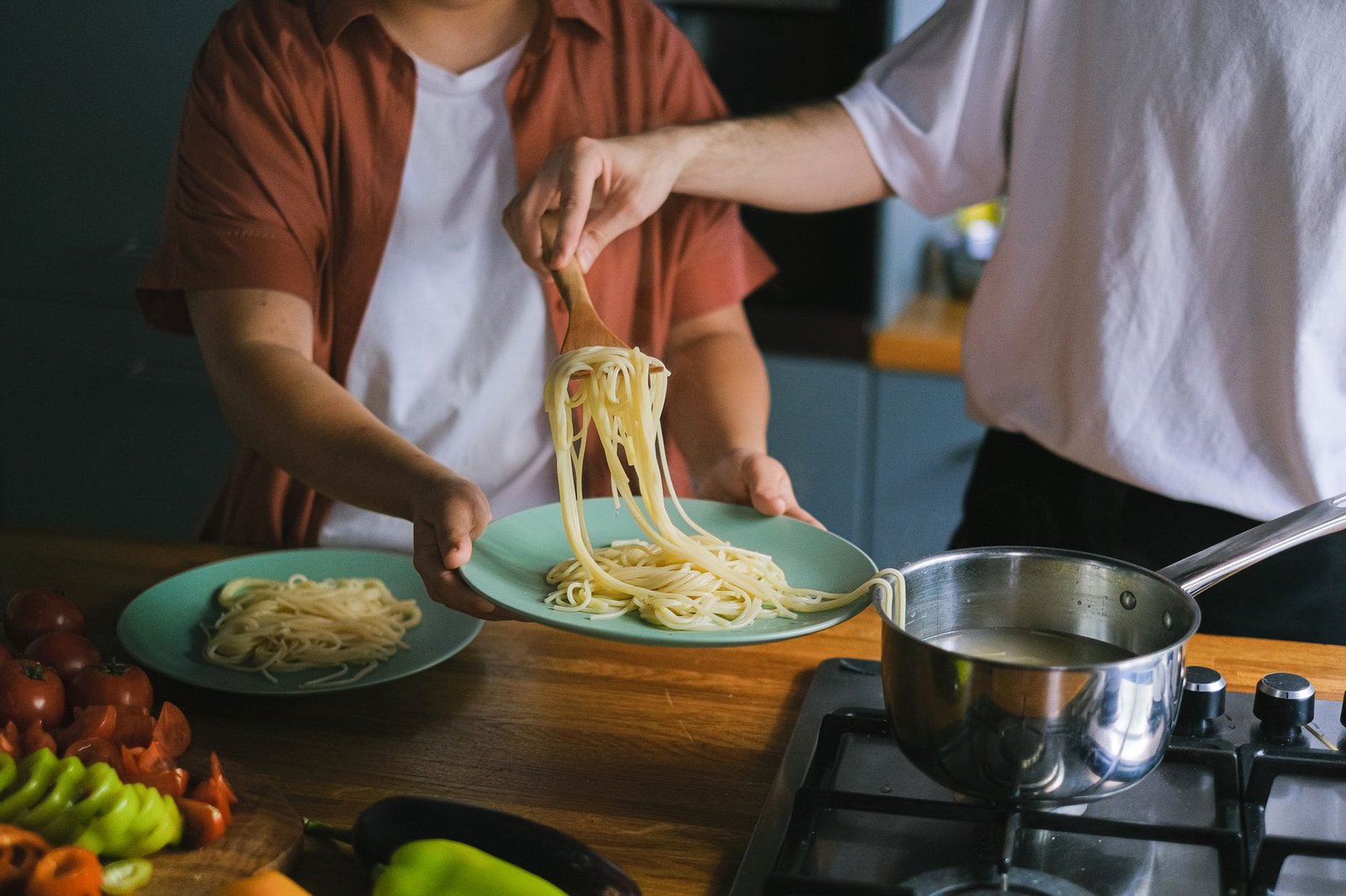 school night dinners — Two adults serving homemade spaghetti onto plates in a cozy kitchen setting.