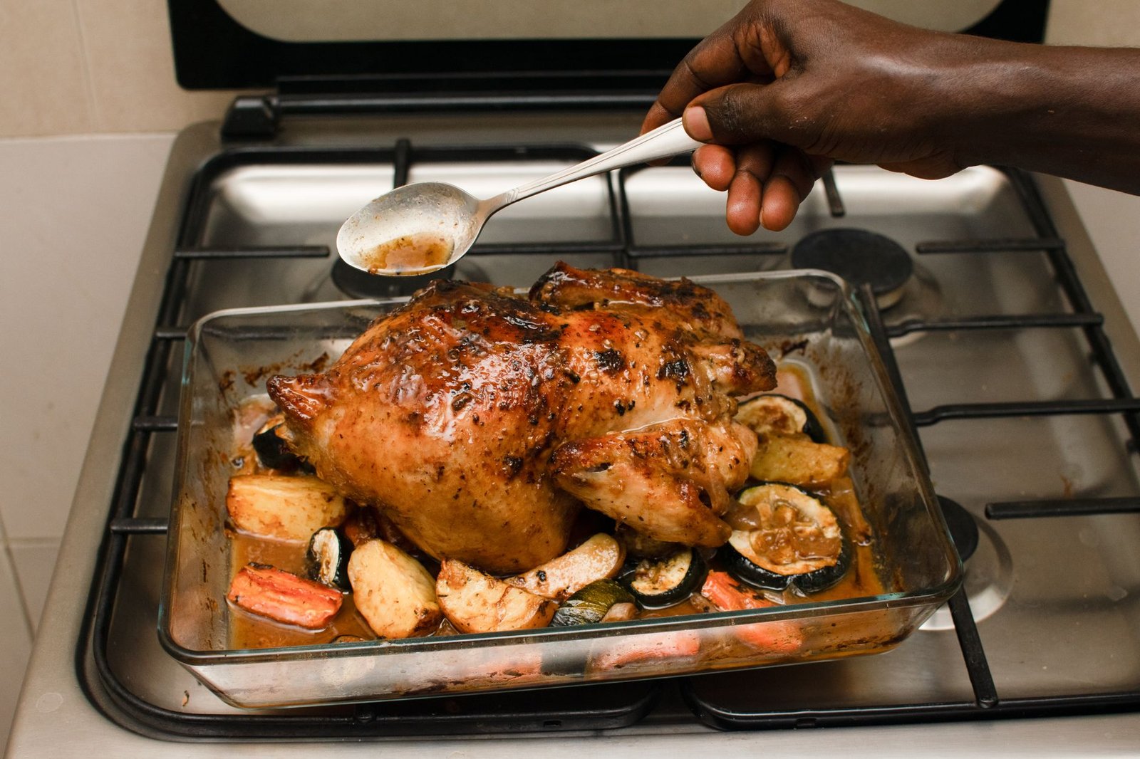 Delicious baked chicken with roasted vegetables being basted in a kitchen setting.