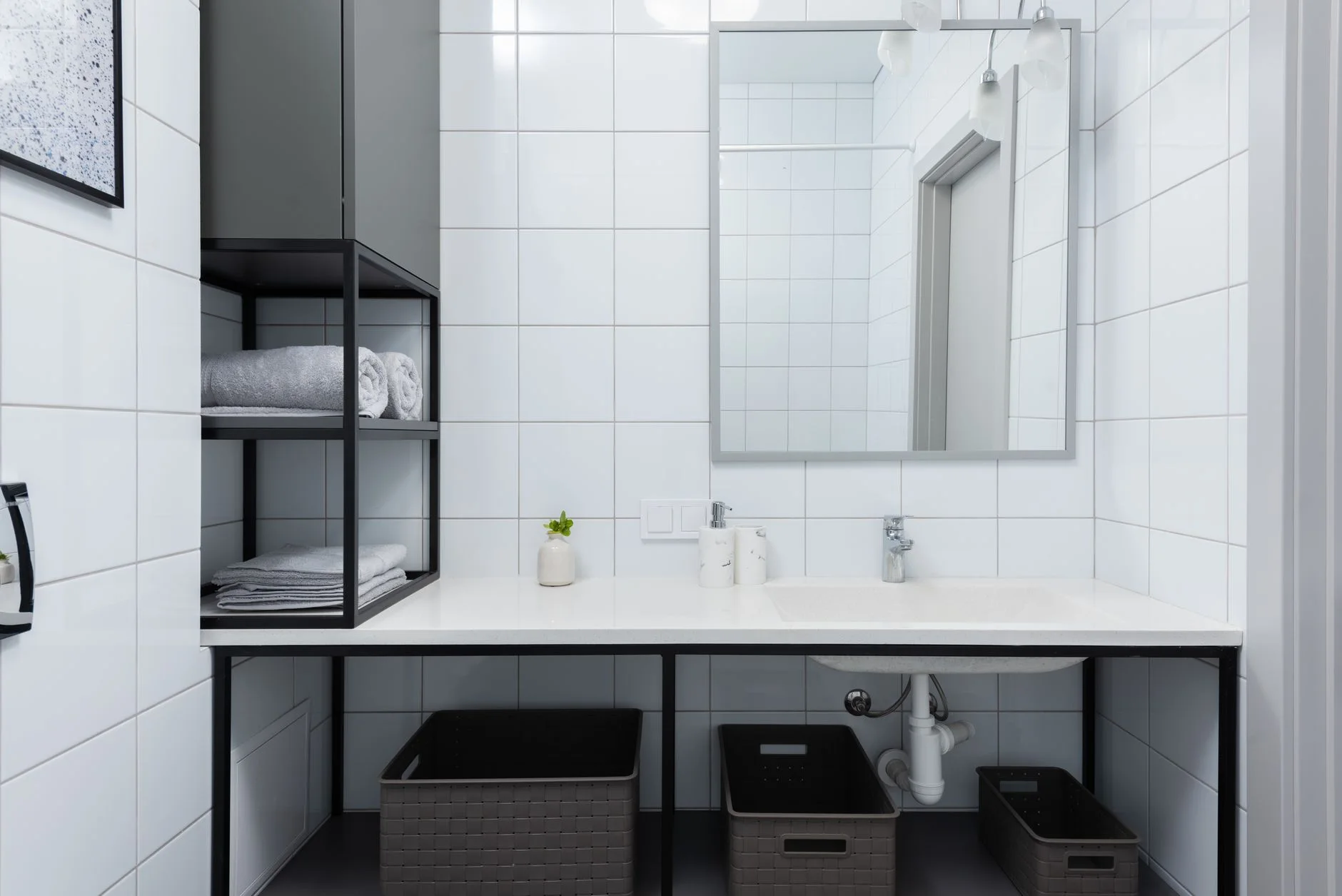 bathroom organization — Interior of light bathroom with white counter near shelves with containers and towels near sink with faucet and mirror on tile near soap