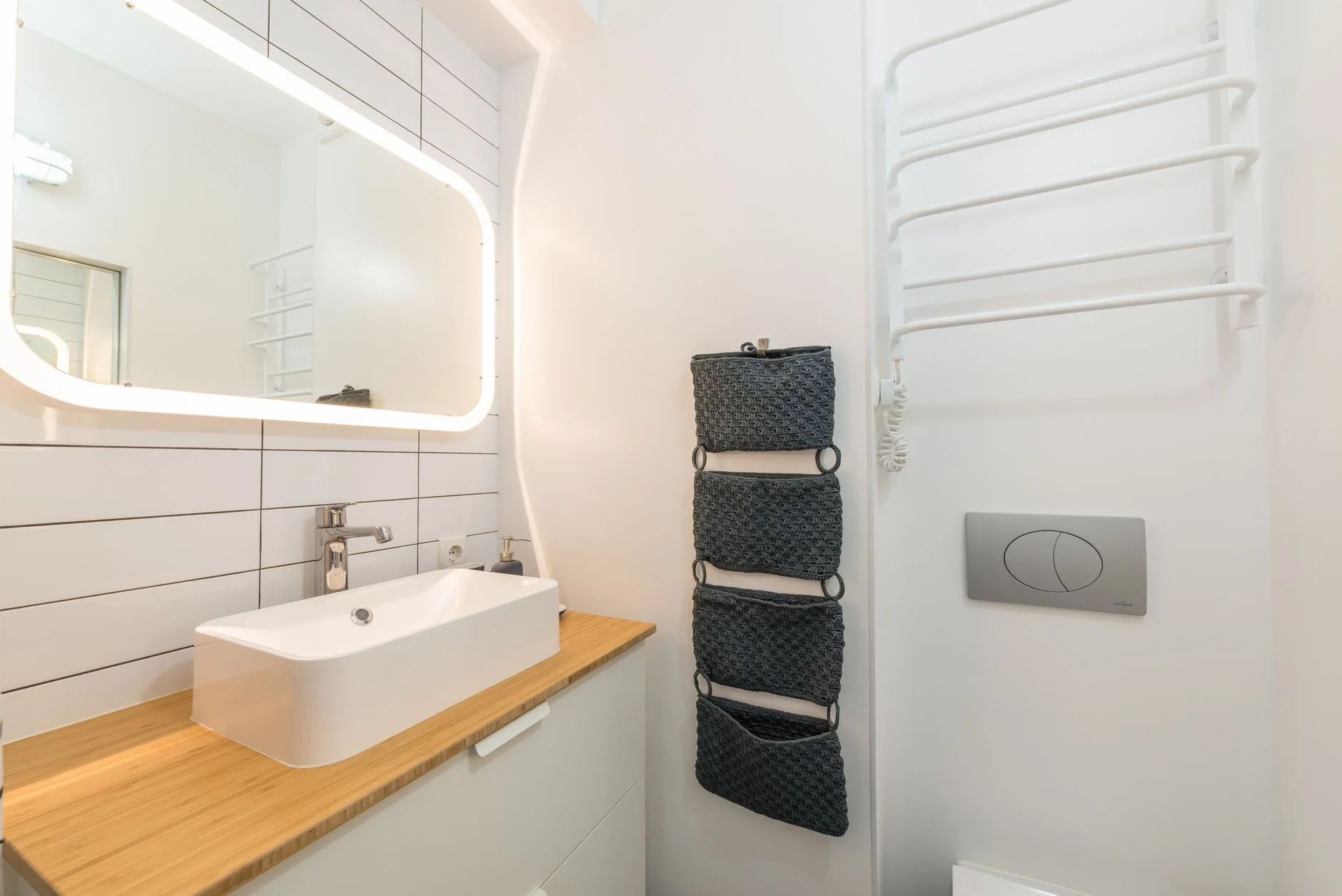 Interior of small modern bathroom with ceramic sink placed on white cabinet with wooden top under illuminated mirror