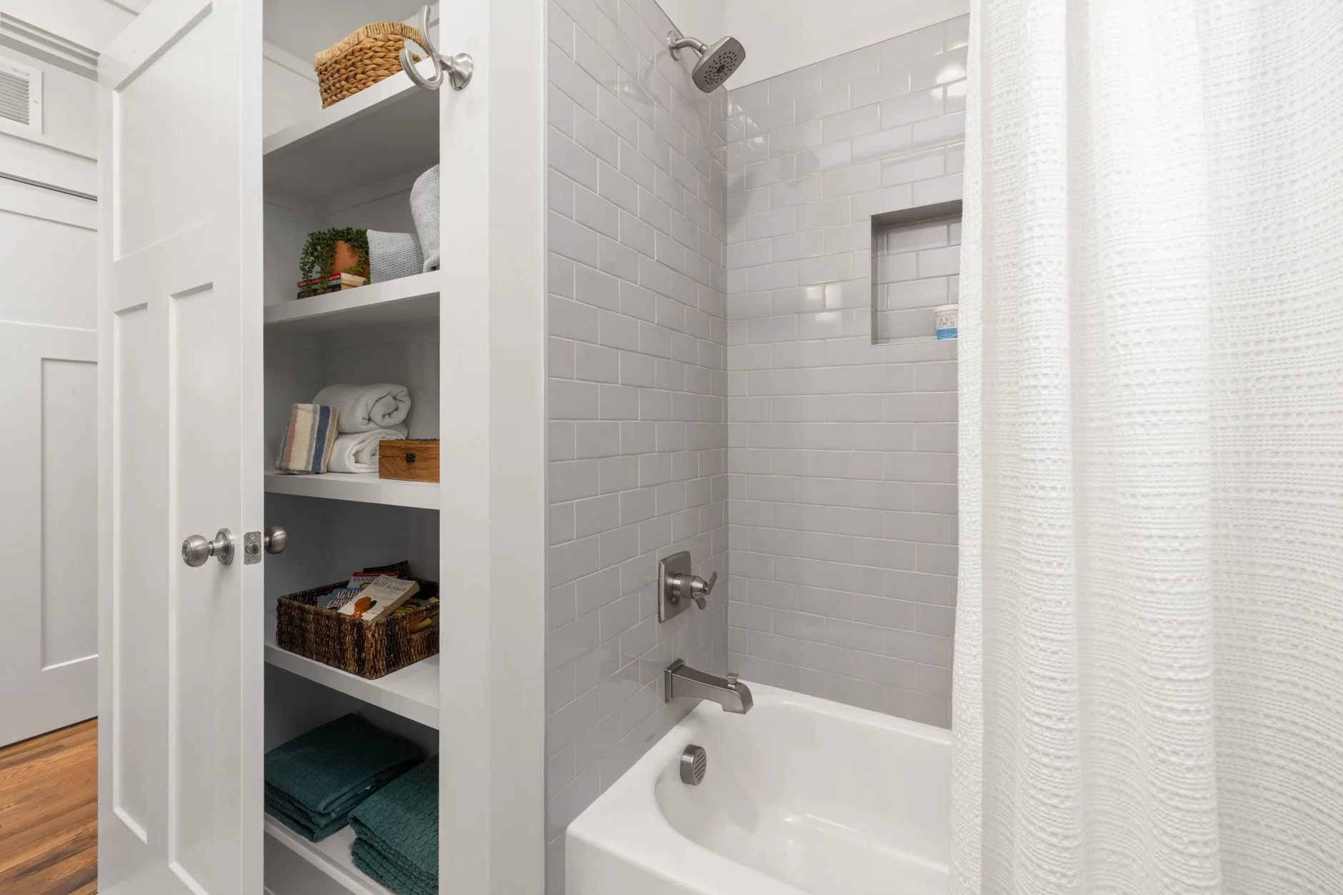 Bright and clean modern bathroom with grey tiles, shower, and organized shelving.