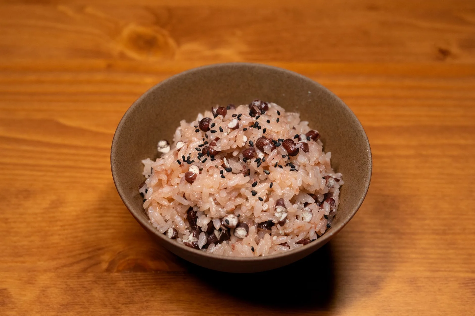 Appetizing bowl of traditional sticky rice mixed with beans and sesame seeds on a wooden surface.