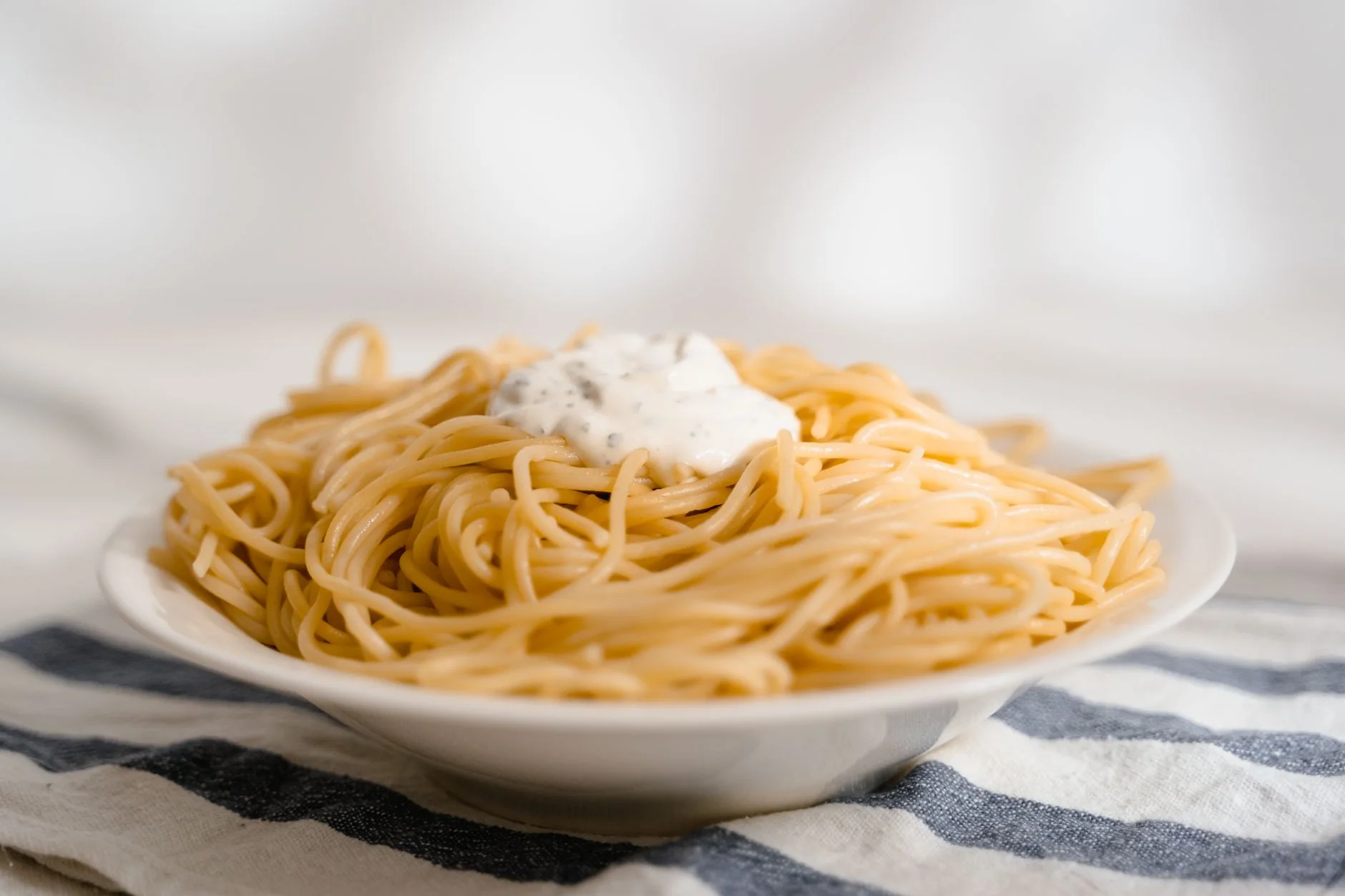 Close-up of a creamy spaghetti dish served on a plate with a white sauce topping.