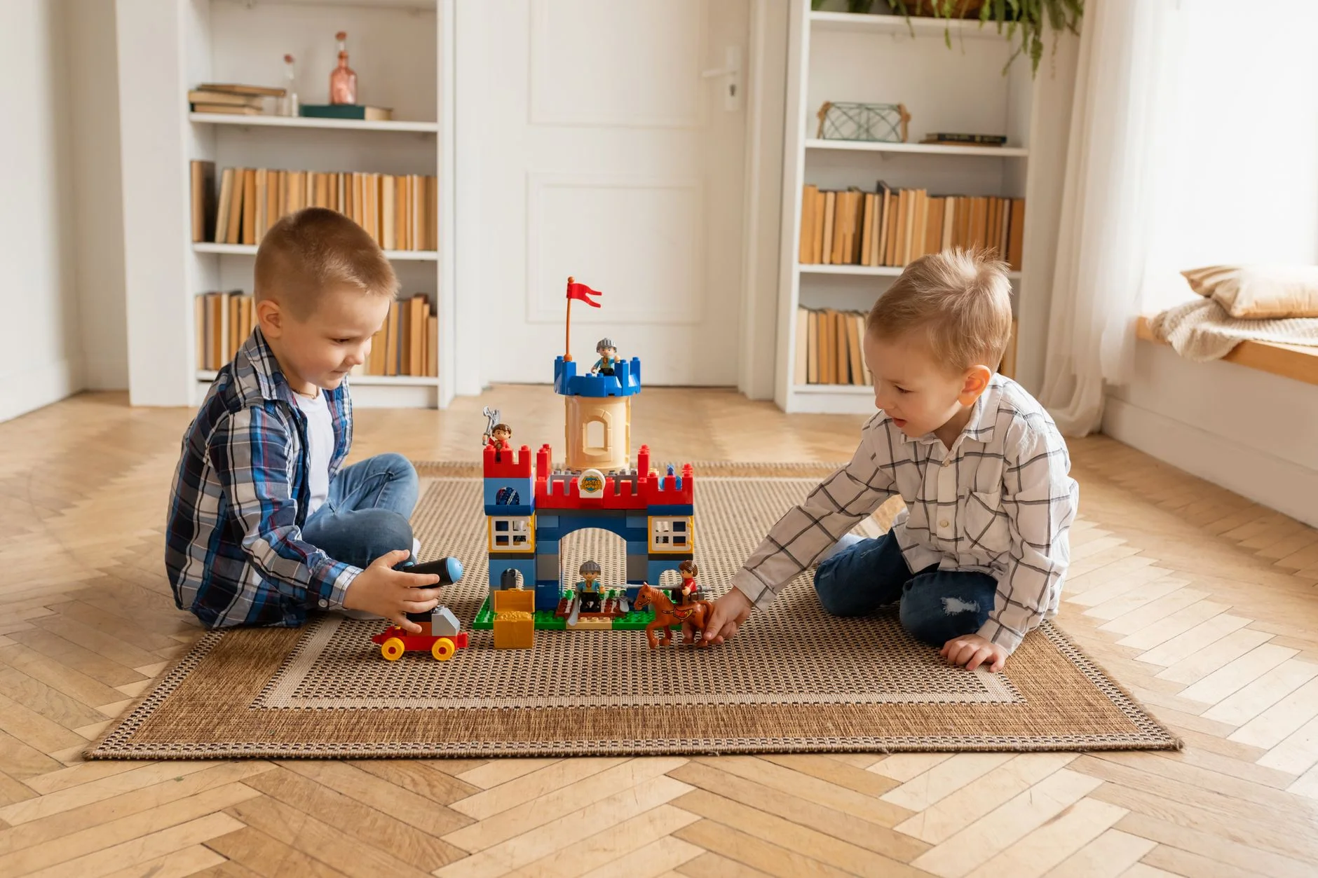 Two young boys enjoying building a colorful toy castle indoors with plastic blocks.