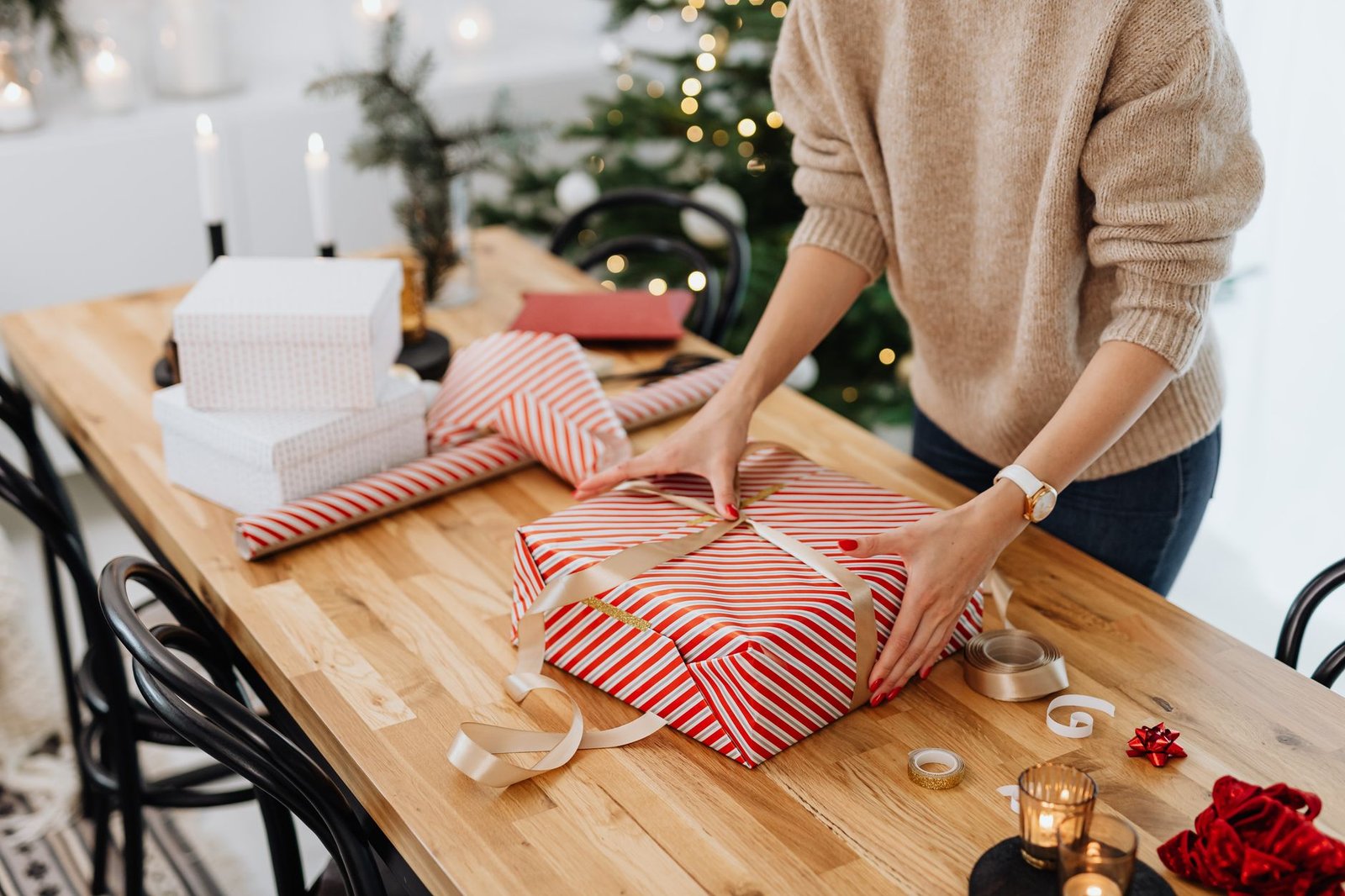 Festive holiday scene of a woman wrapping Christmas presents on a wooden table indoors.