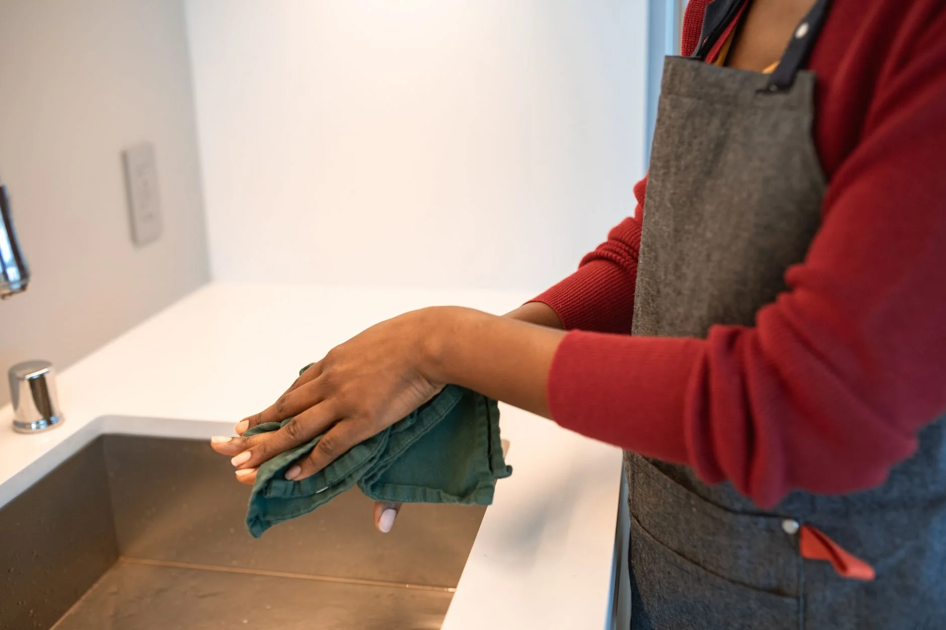 Close-up of a person cleaning hands with cloth by a kitchen sink indoors.
