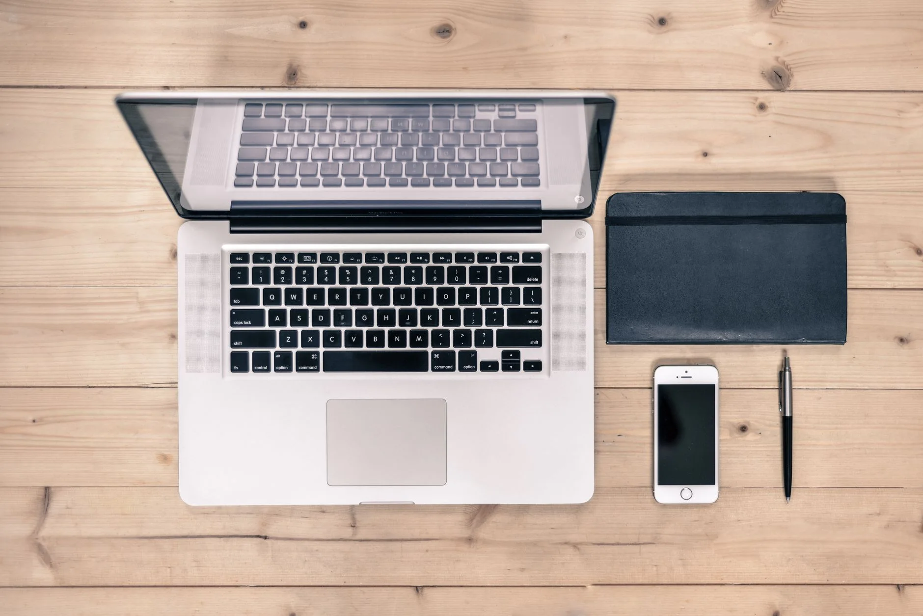digital declutter — Top view of a tidy workspace featuring a laptop, smartphone, notebook, and pen on a wooden desk.