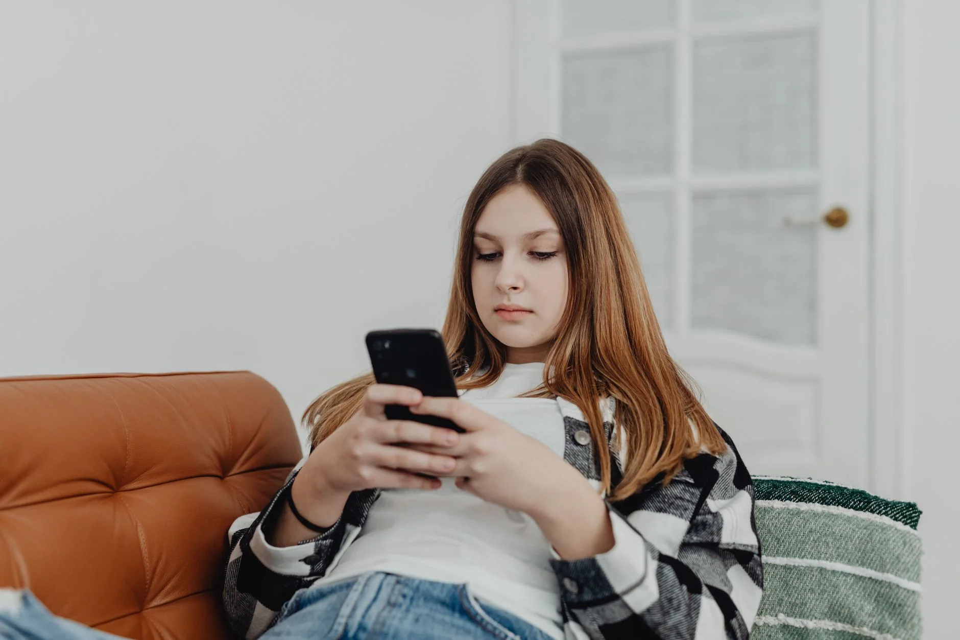 Teenage girl using smartphone while lounging on a sofa indoors.