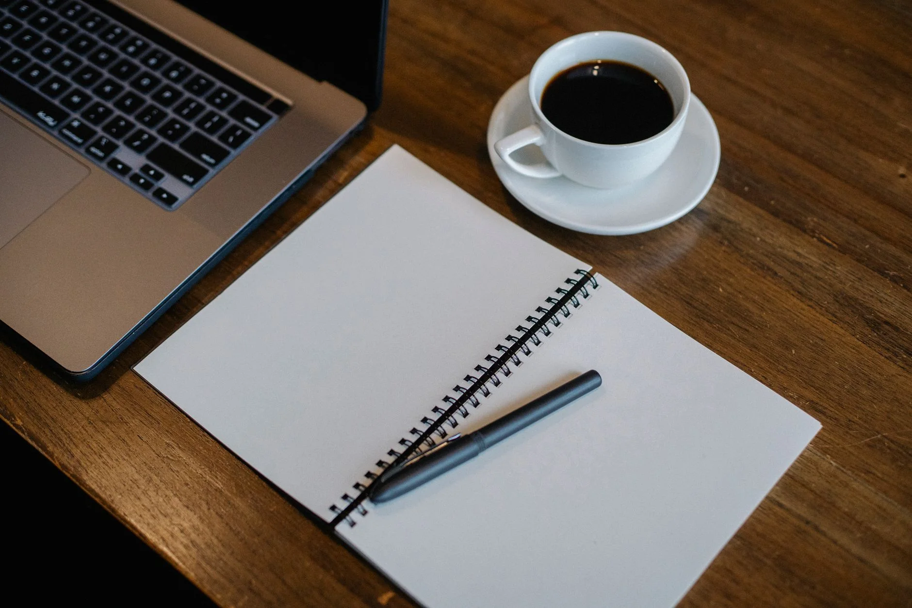 From above of workspace with cup of hot coffee and pen on empty notepad near modern laptop on wooden table