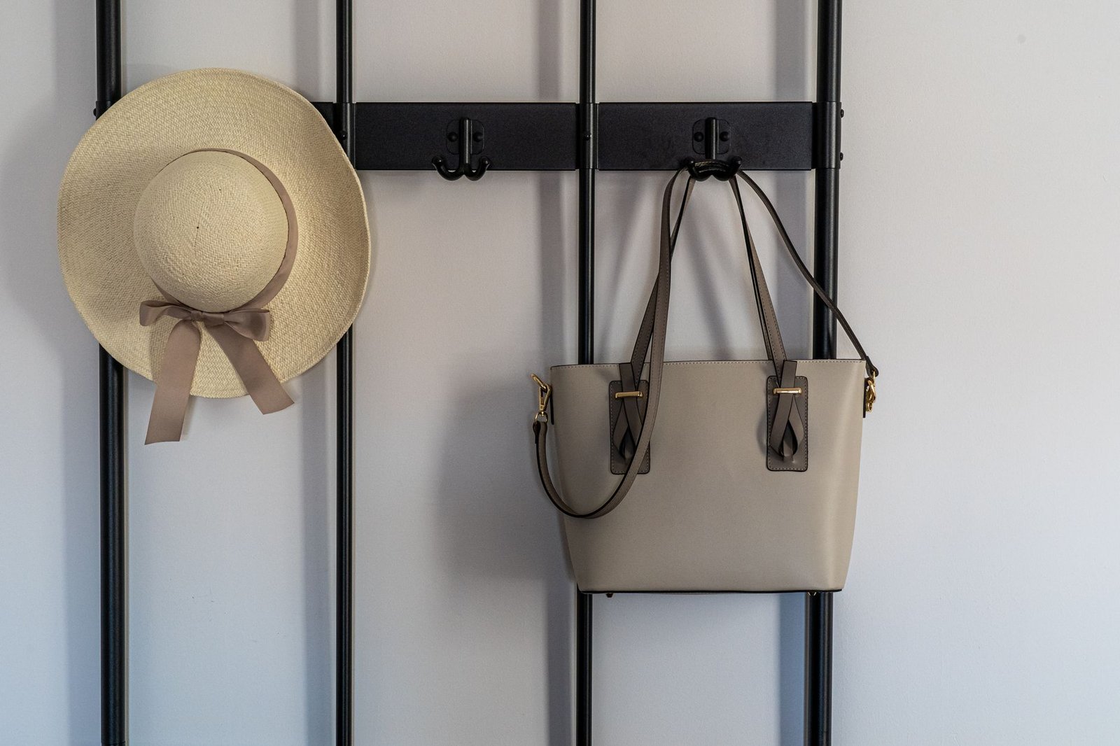 A stylish sun hat and leather handbag hanging on a modern wall hook indoors.