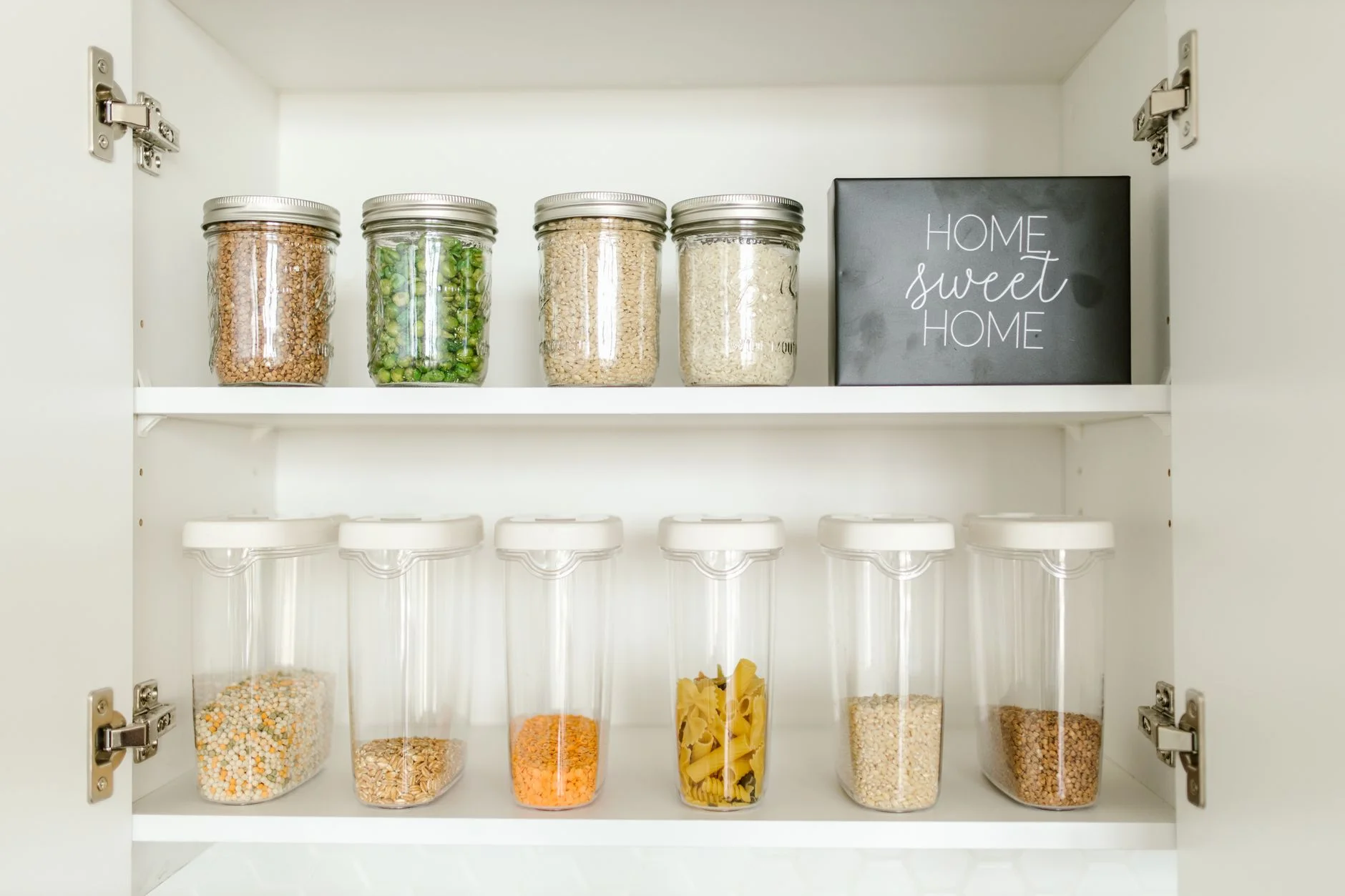 fridge organization — Neatly arranged glass and plastic jars containing grains and pasta in a kitchen cabinet.