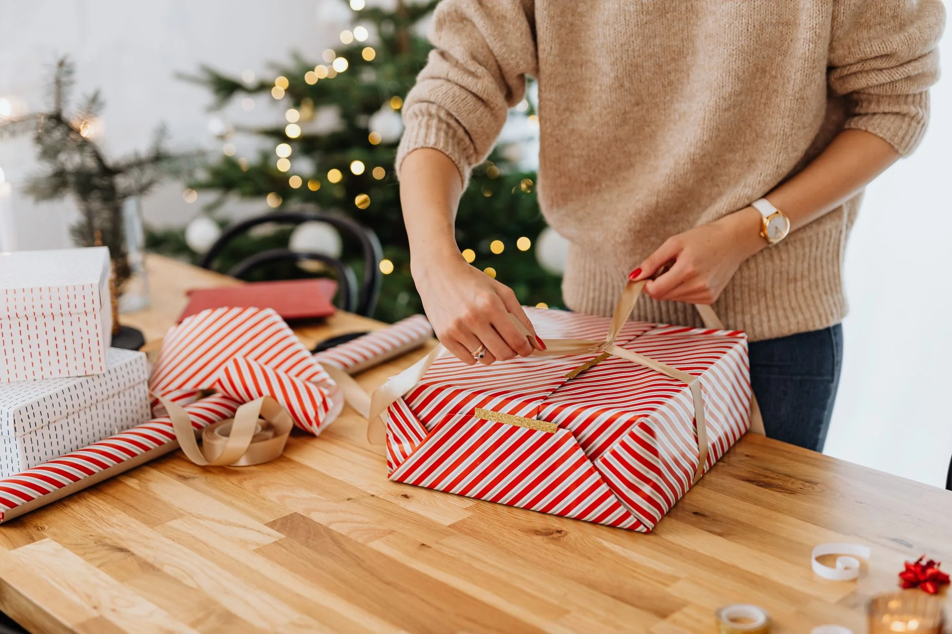 gift wrapping station — A woman wrapping gifts by a Christmas tree, spreading holiday cheer.