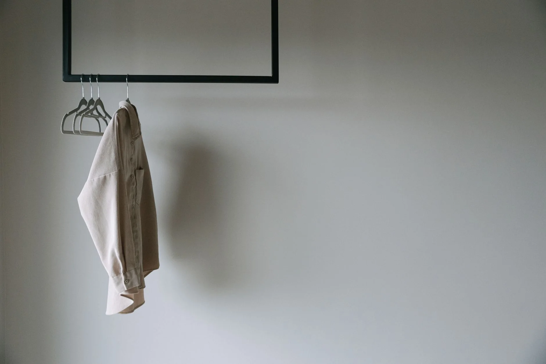 capsule wardrobe — A beige blazer hangs on a minimalist metal rack, providing a serene and stylish wardrobe aesthetic.
