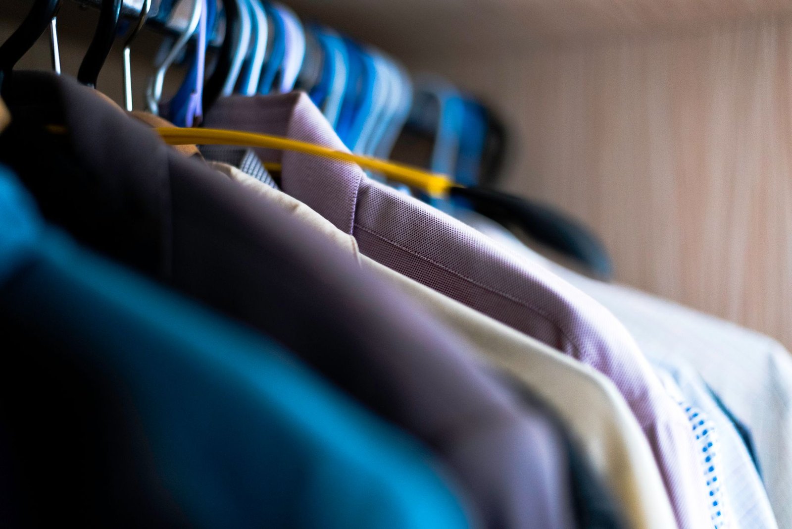 how to declutter your closet — Close-up of various shirts hanging on colorful hangers inside a wardrobe.