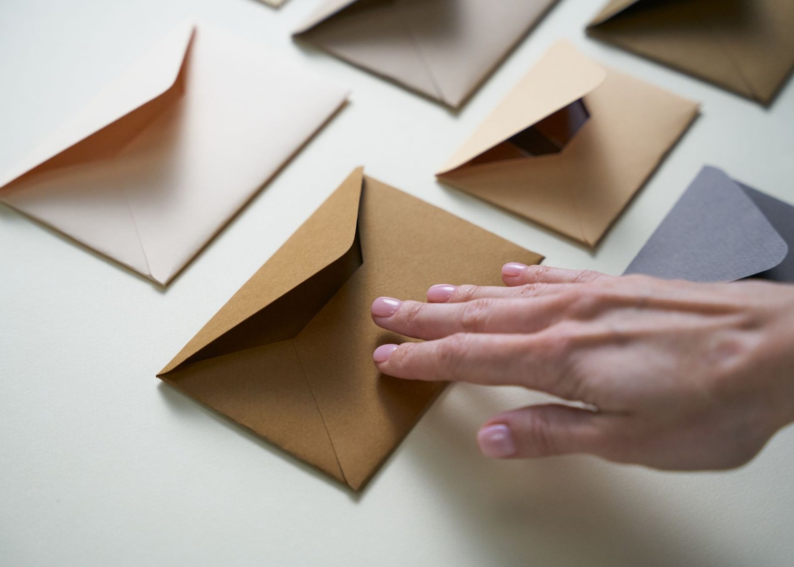A hand gently touches brown envelopes spread on a white surface, illustrating organization.