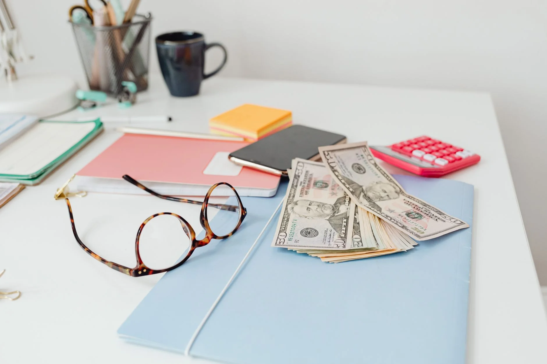 how to pay off debt — Office desk setup with eyeglasses, dollar bills, and stationary items. Perfect for finance or business themes.
