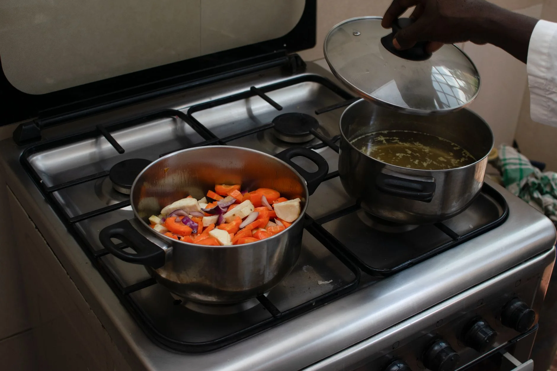 A kitchen scene featuring fresh vegetables being cooked in pots on a gas stove.
