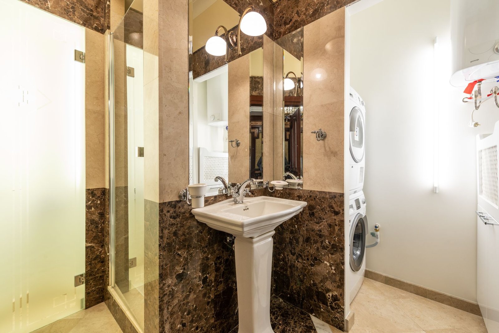 Elegant bathroom interior featuring marble walls, a pedestal sink, and a washer-dryer unit.
