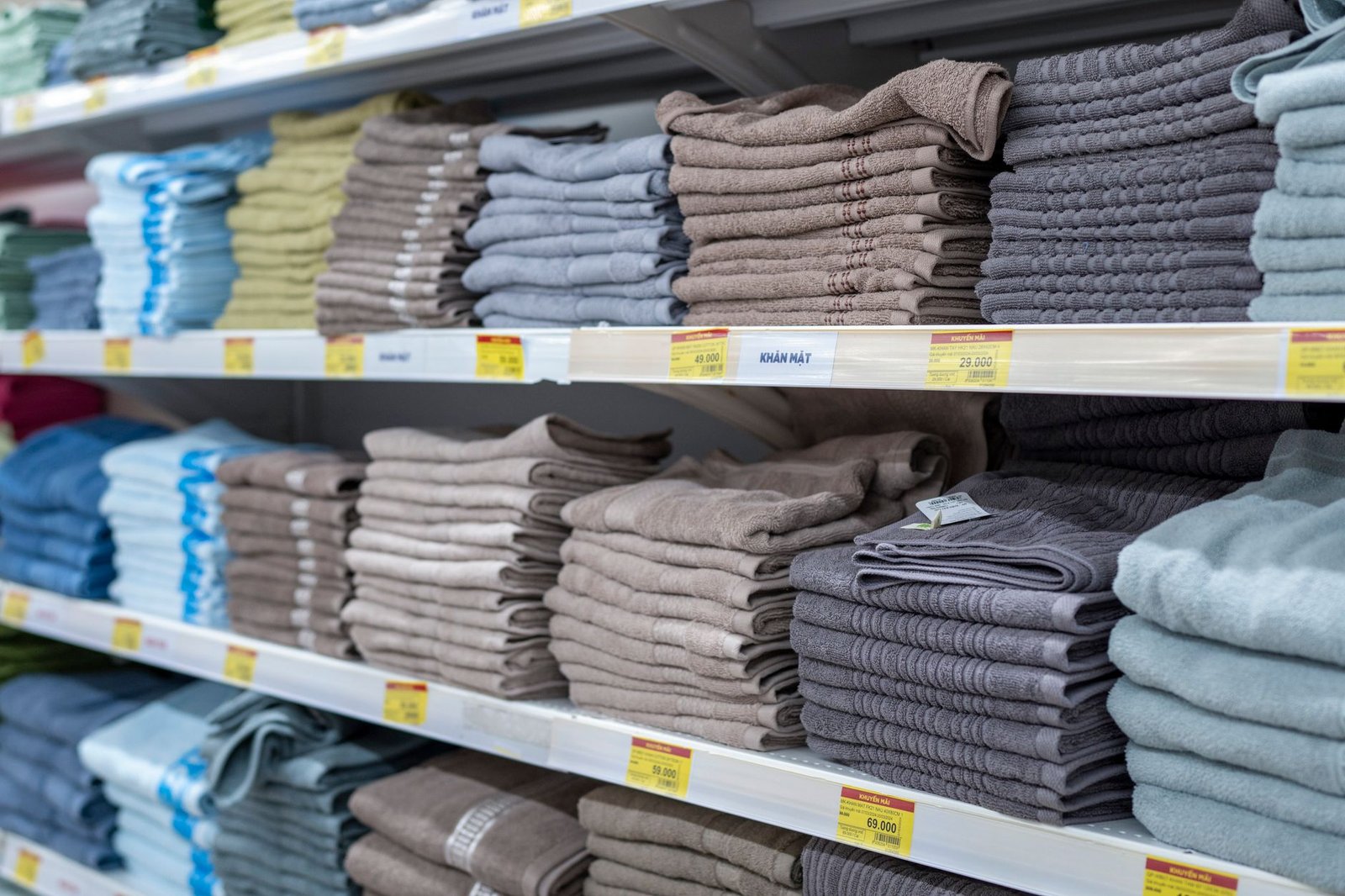 Neatly folded towels in various colors stacked on retail shelves inside a store.