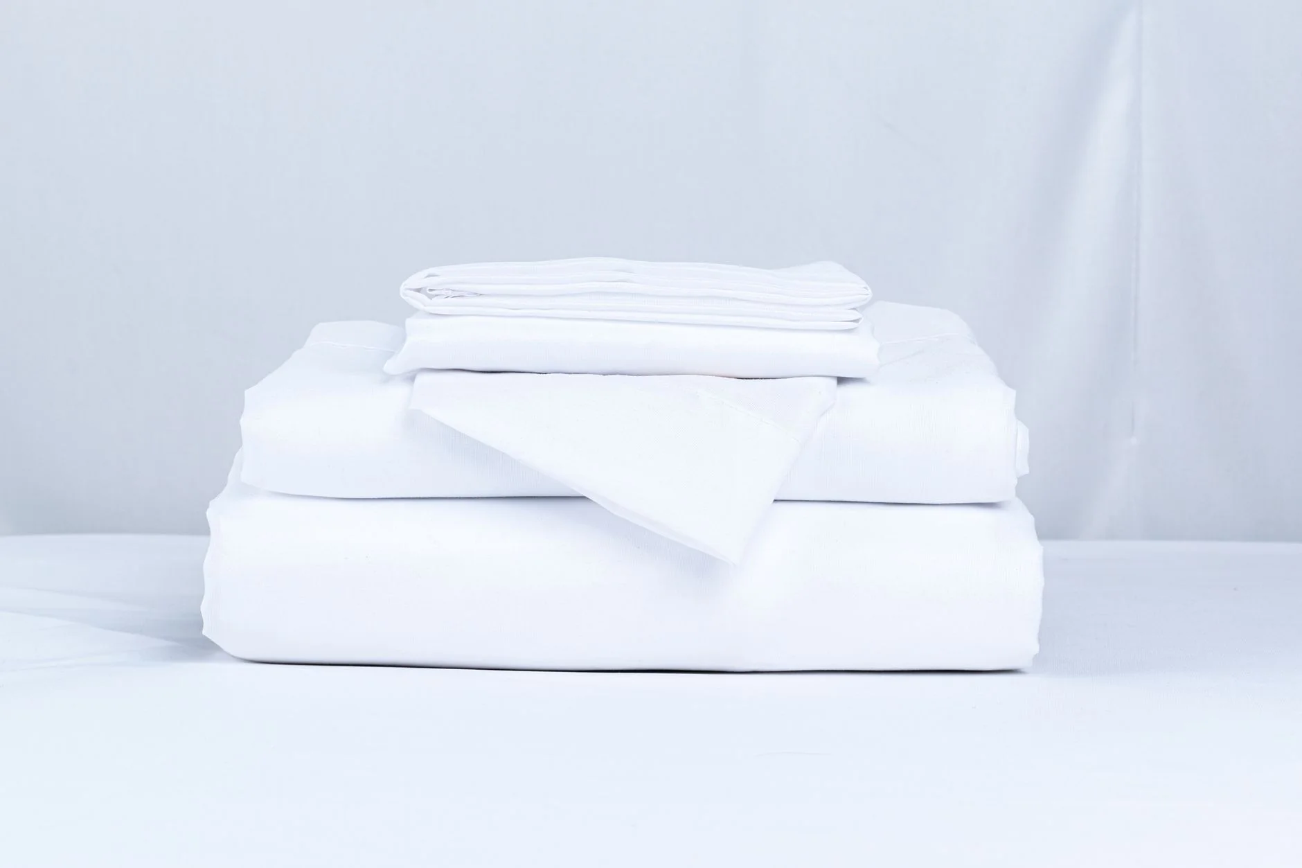 A neatly folded stack of crisp white bed linens on a clean surface.