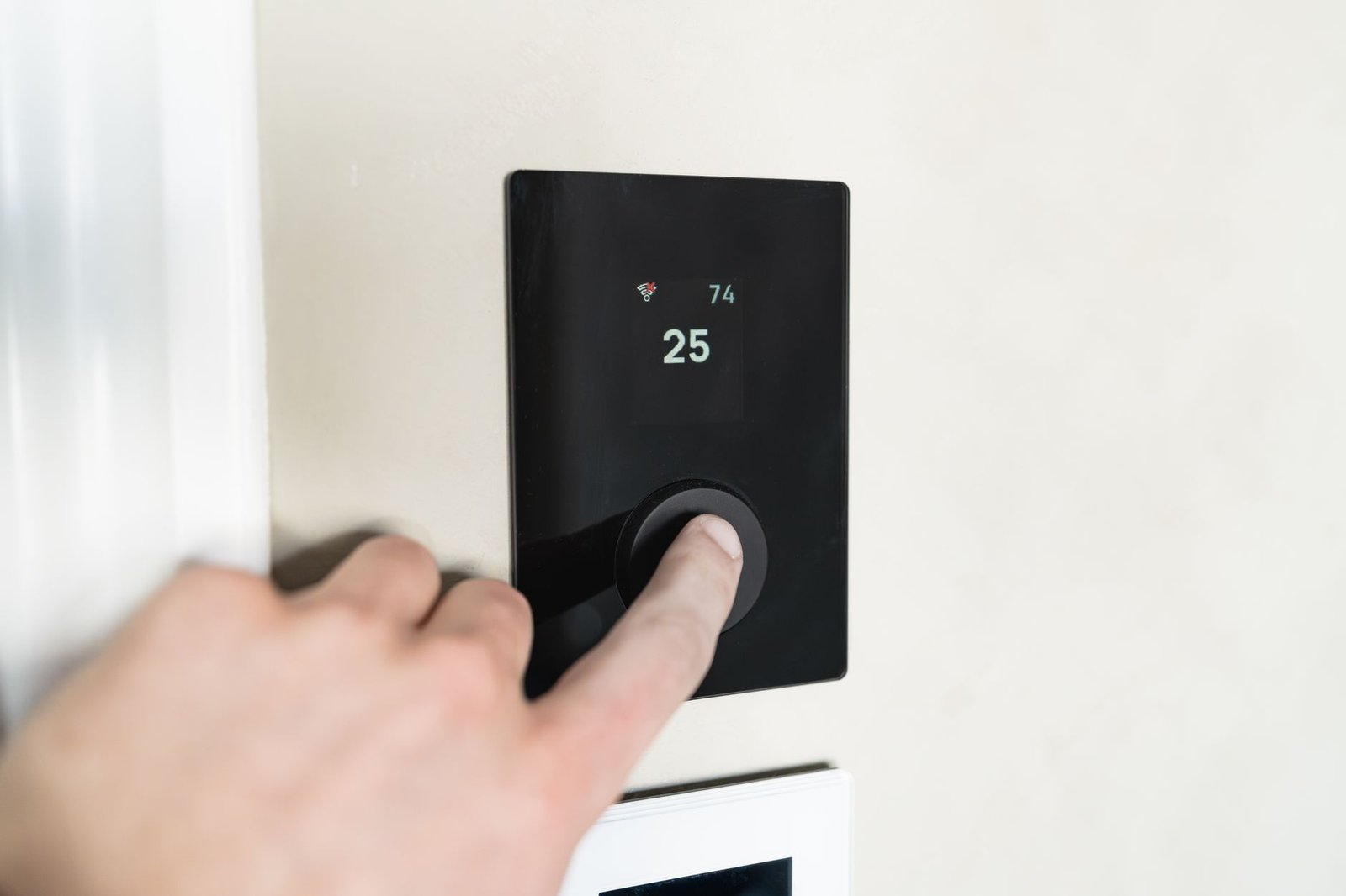 lower heating bill — Close-up of a hand adjusting a sleek, modern smart thermostat on a wall.