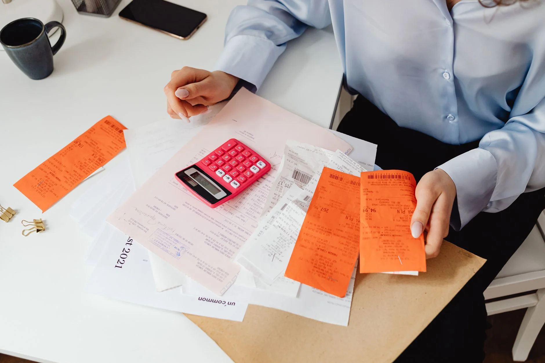 lower your household bills — A woman reviews receipts and calculates expenses at a desk with a pink calculator.