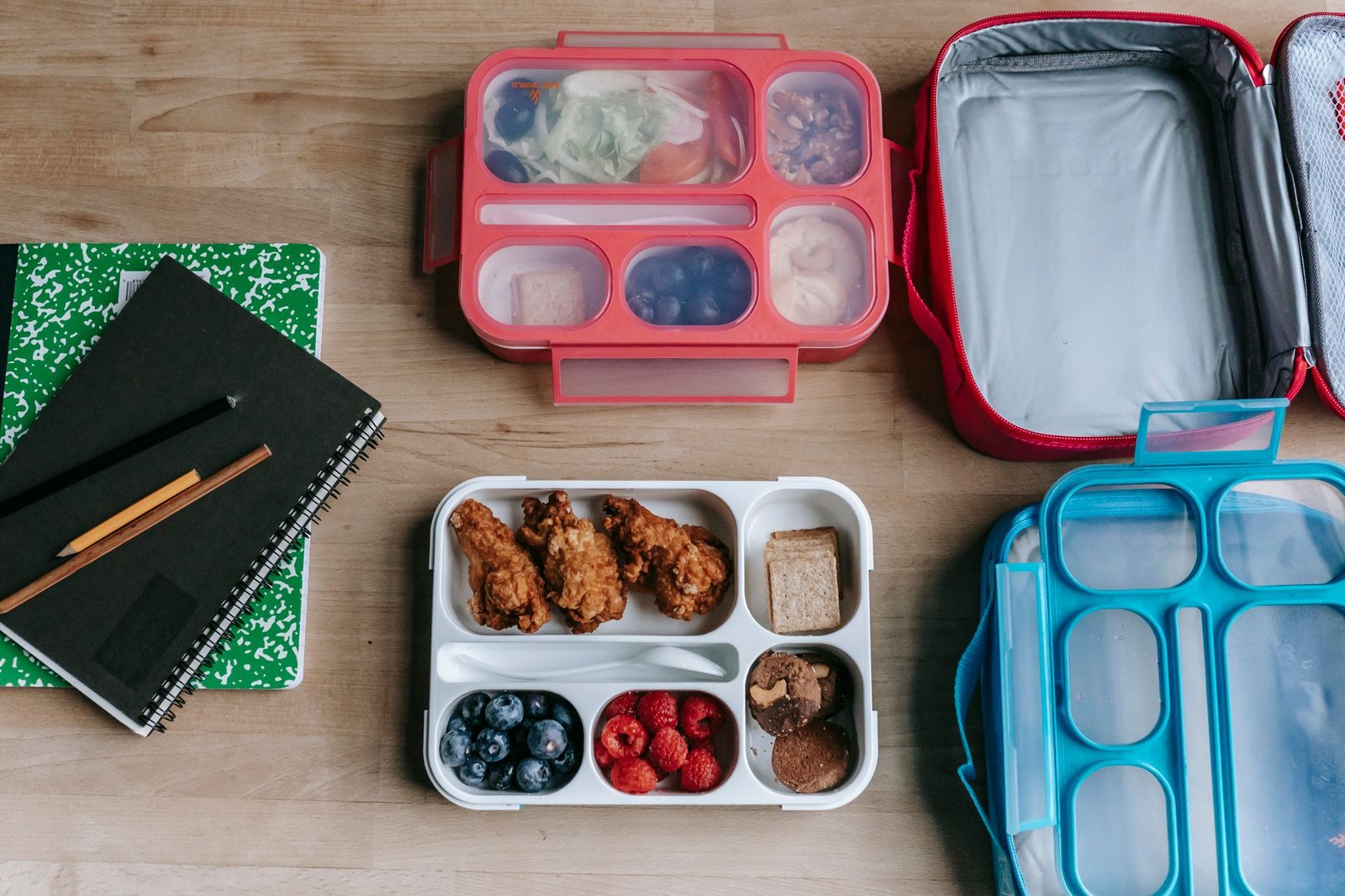 lunchbox ideas — Top view of composed plastic lunchboxes near copybooks under pencils on wooden table