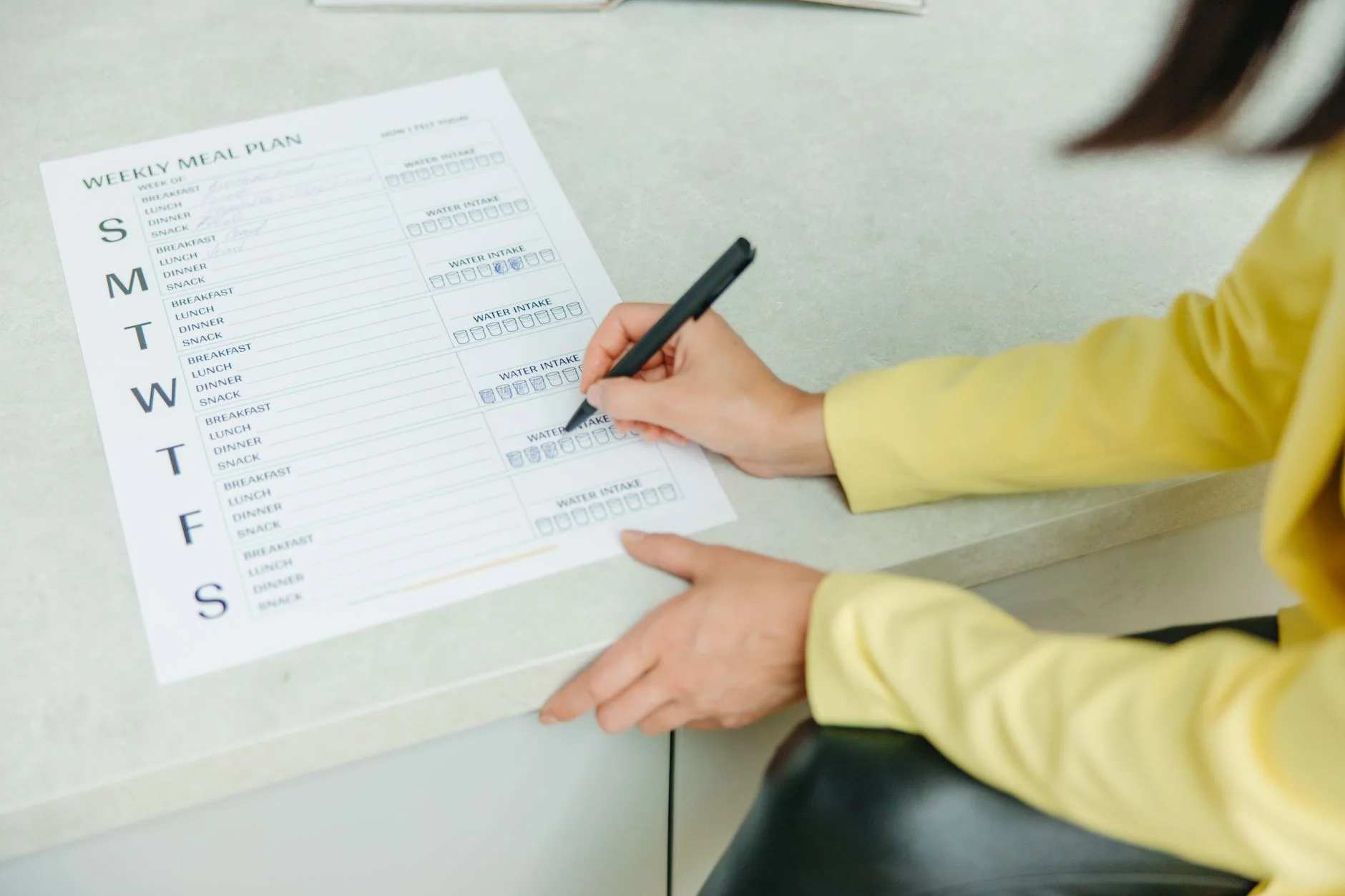 meal planning for beginners — Woman writing on a weekly meal plan checklist indoors, focusing on diet organization.