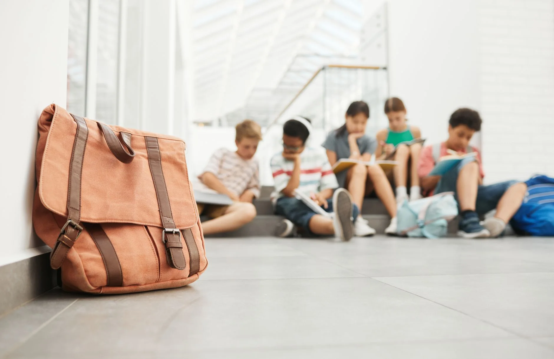 school morning routine — Tan leather bag in focus with students studying in the background.