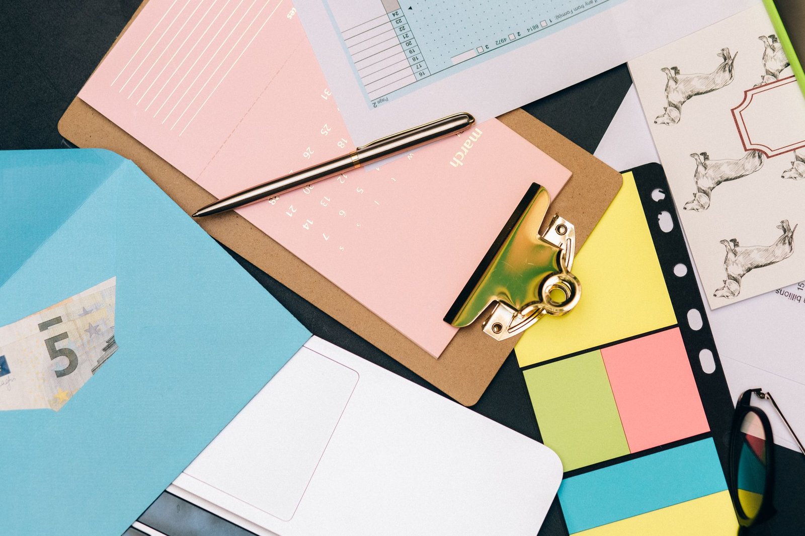 Neatly arranged desk supplies with clipboard, euro bill, and colorful notes.