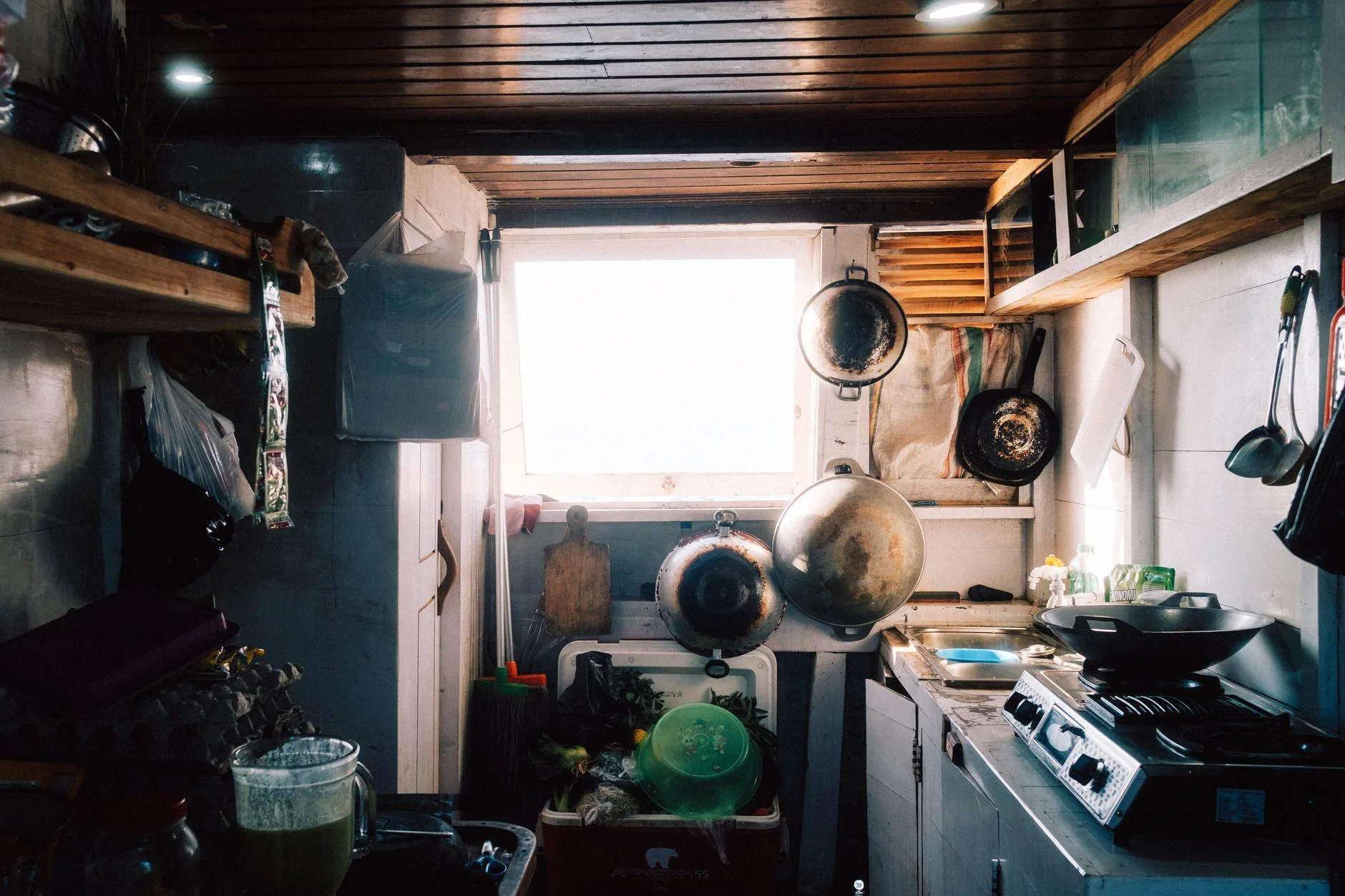 Cozy rustic kitchen featuring hanging pans, woks, and natural lighting through a window.