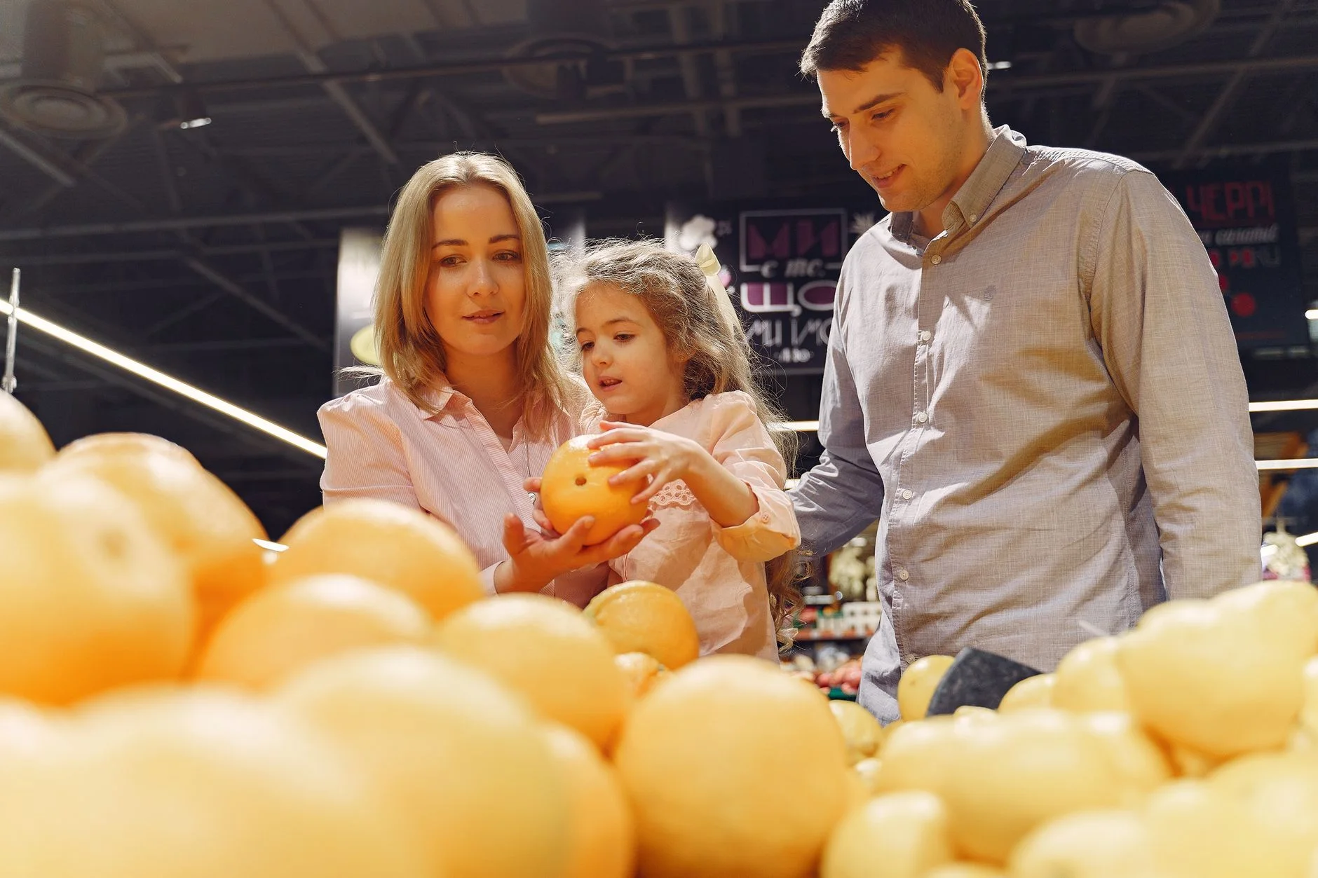 Parents and child selecting fresh oranges together at the supermarket. Captures family bonding and healthy shopping.