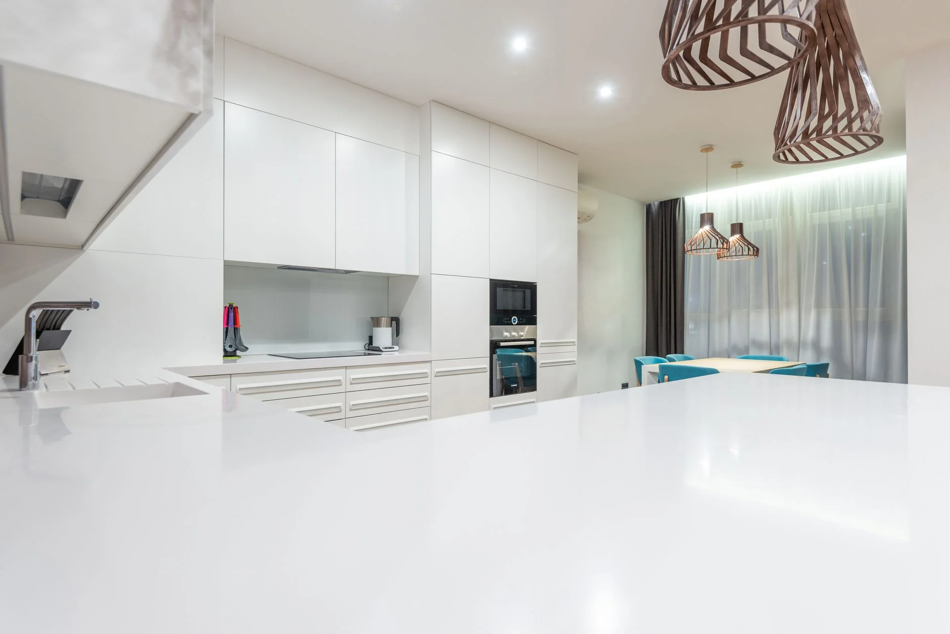 Empty kitchen counter against white cupboards and modern appliances near chairs at table placed near window in spacious stylish apartment