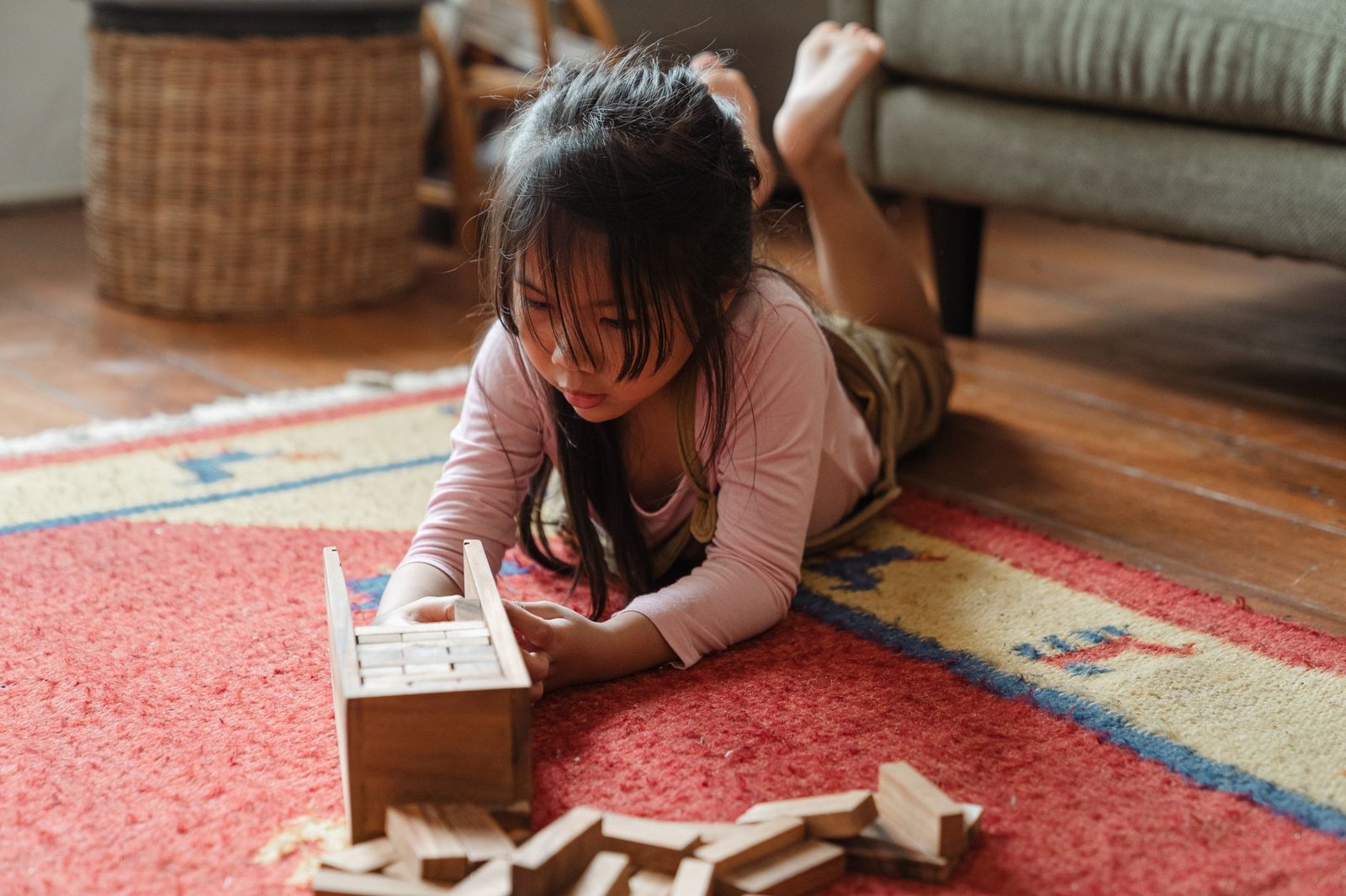 Young girl enjoying playtime with wooden blocks on a colorful carpet in a cozy living room.