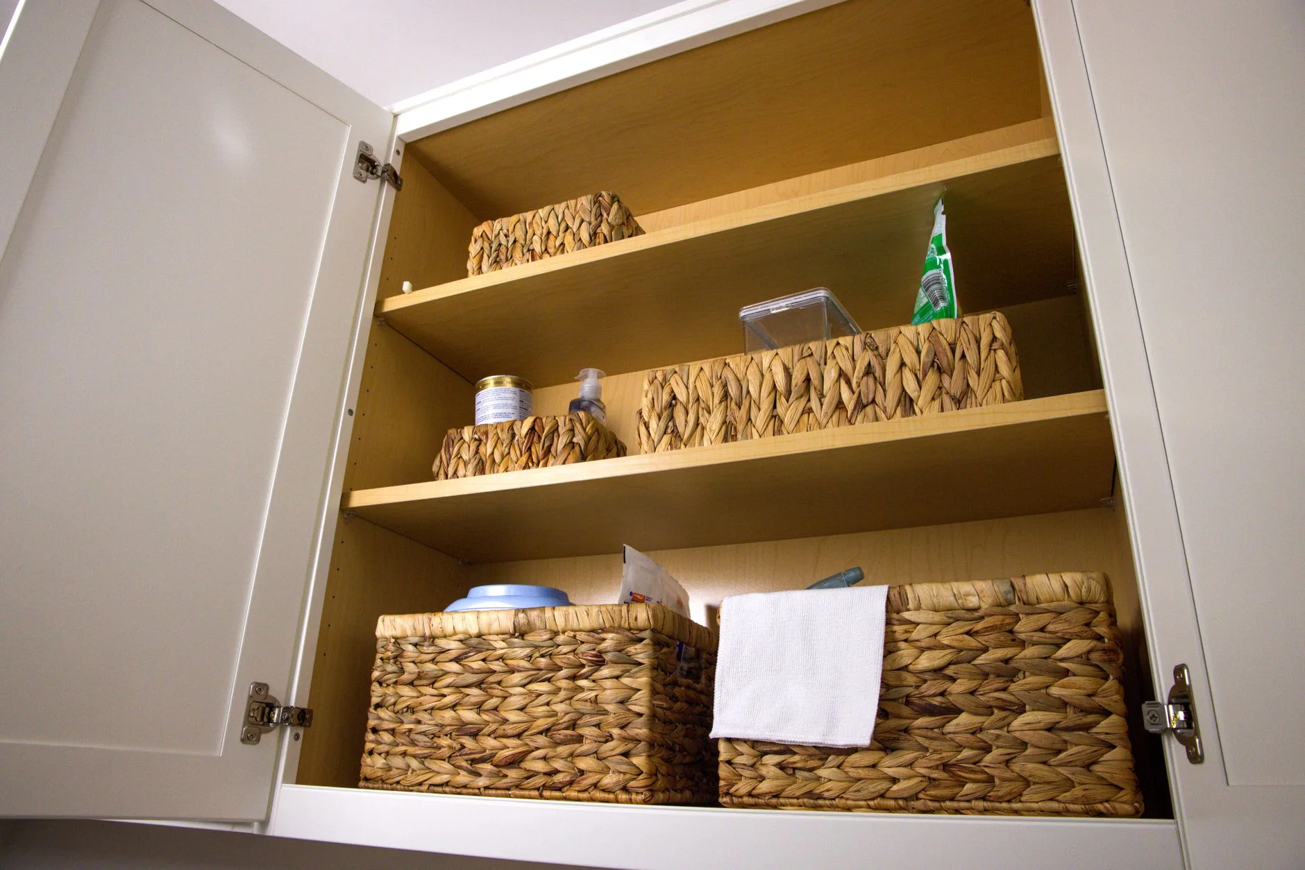 under sink organization — Neat storage in a kitchen cabinet using wicker baskets for a clean aesthetic and organization.