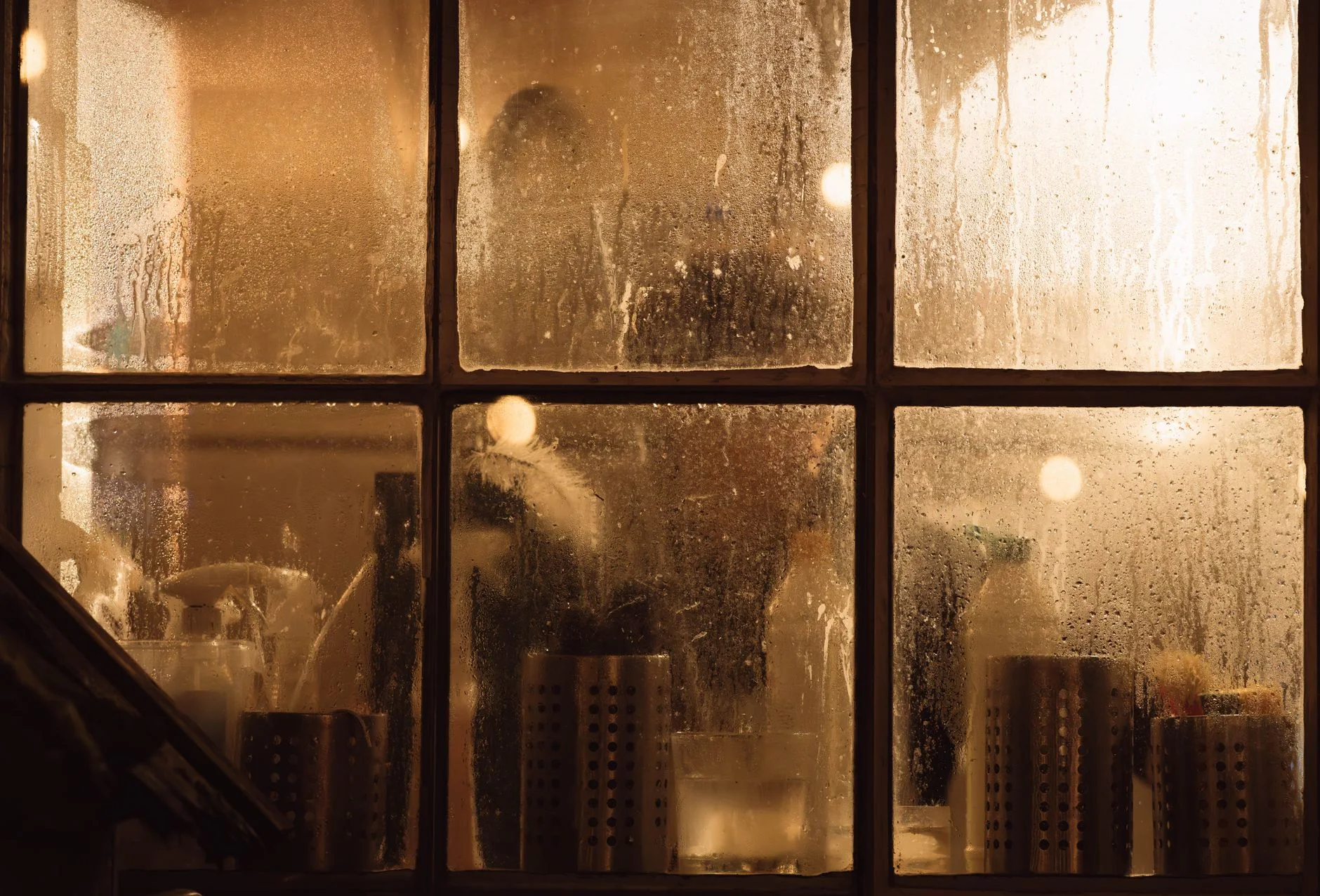 Moody view through a fogged window into a cozy interior with warm lighting.